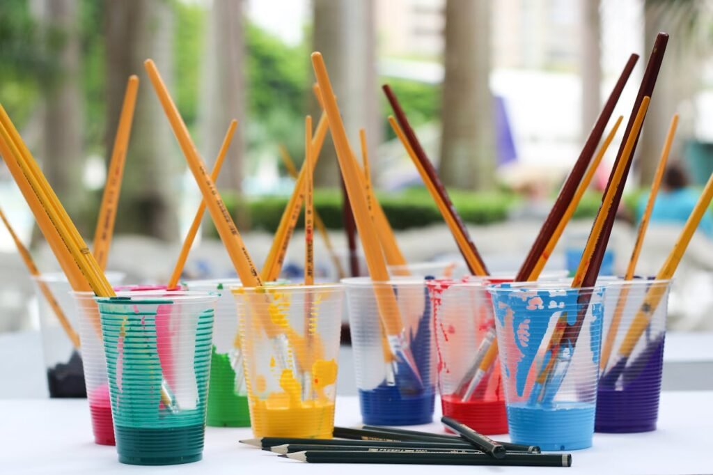 image of paint brushes in cups filled with different colour paint