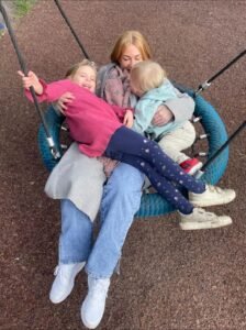 picture of a mother on a swing with young girl and baby boy