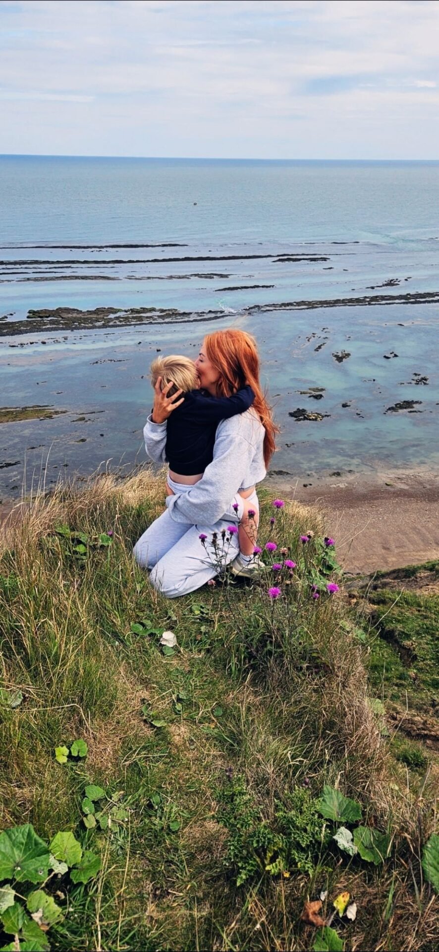 Jen embracing her child by the coast